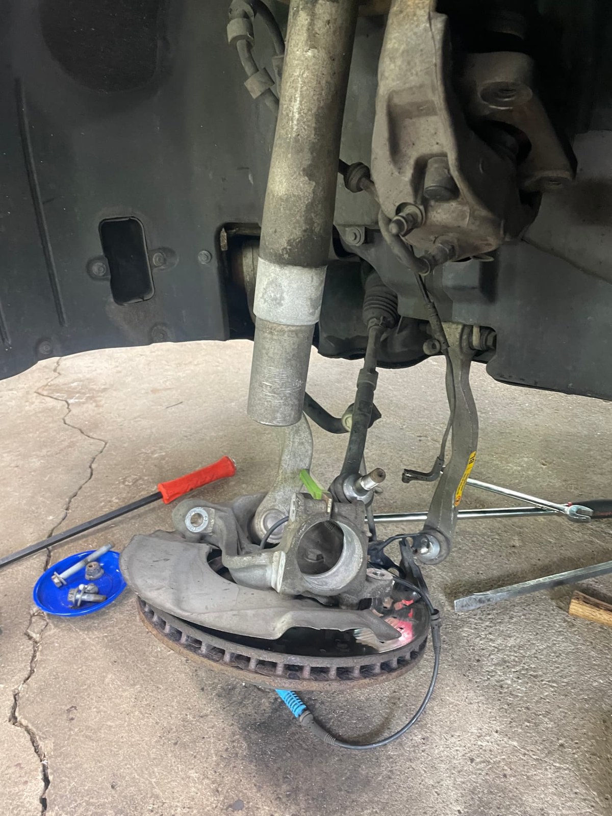 Front suspension teardown with steering knuckle, control arms, and brake rotor removed during a repair