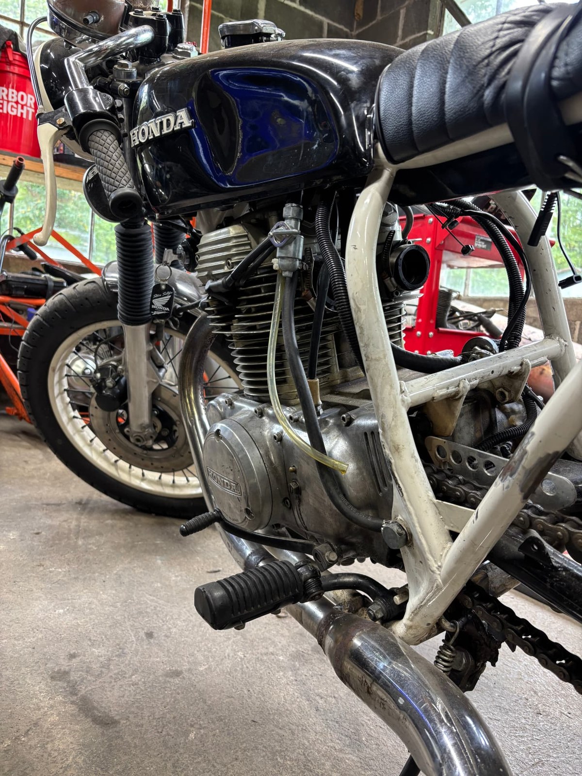 Vintage Honda motorcycle with its fuel tank and carburetor exposed during a repair