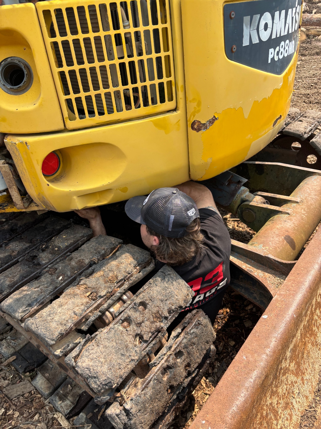 G23 technician performing rear-end maintenance on a Komatsu PC88MR excavator in the field