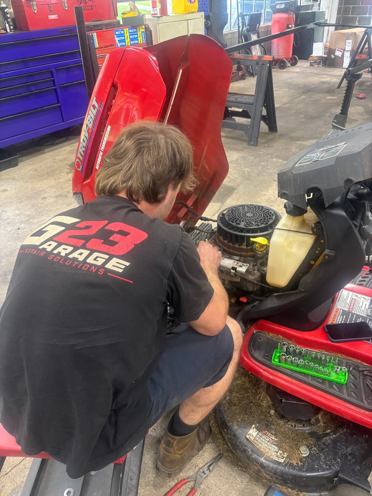 G23 technician repairing the engine of a red Troy-Bilt riding lawn tractor in the shop