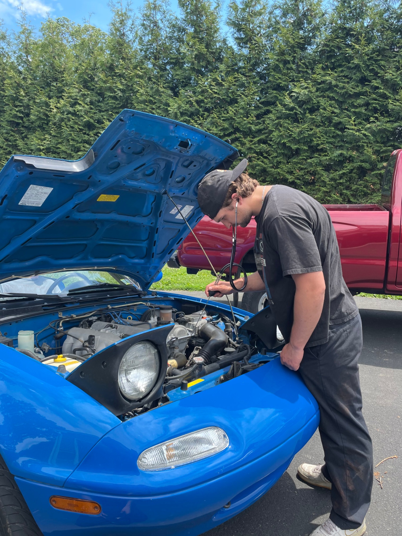 Mechanic using a stethoscope to diagnose engine noise on a blue Mazda Miata