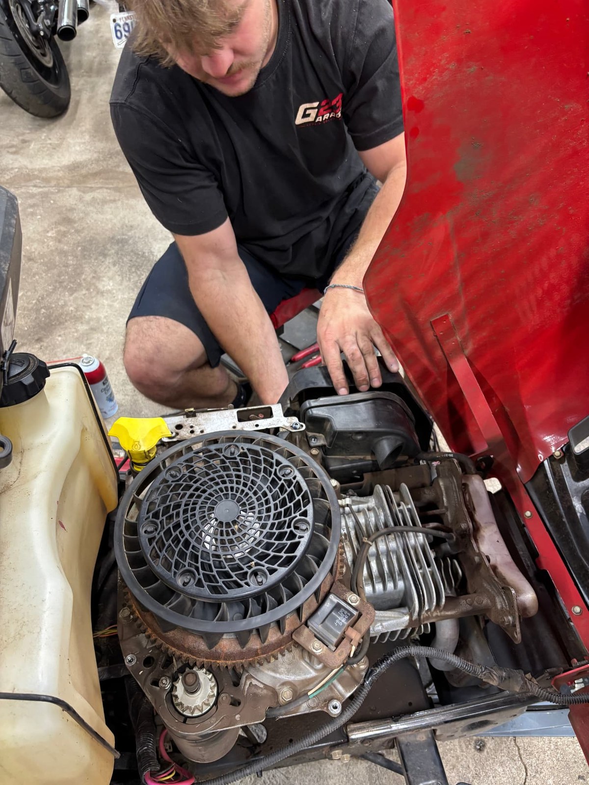 G23 technician servicing the engine of a riding lawn mower with the hood open
