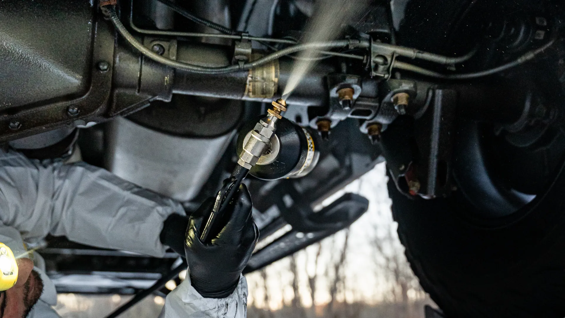 Technician spraying undercoating onto a vehicle undercarriage for corrosion protection