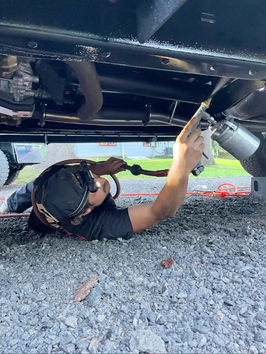 Technician spraying undercoating onto a truck underbody with a spray wand