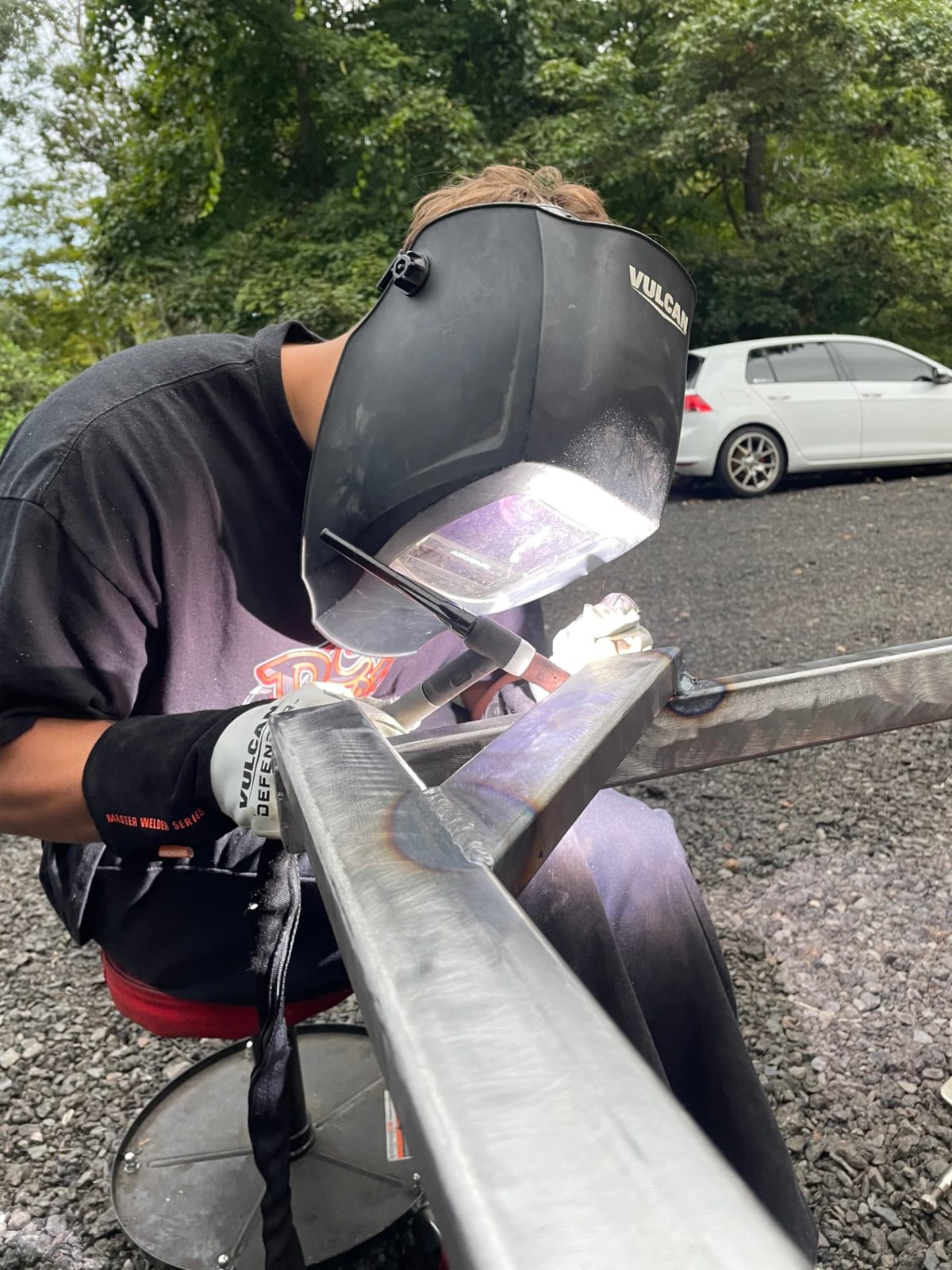 Technician in a welding helmet TIG welding a joint on a square tube steel gate frame outdoors