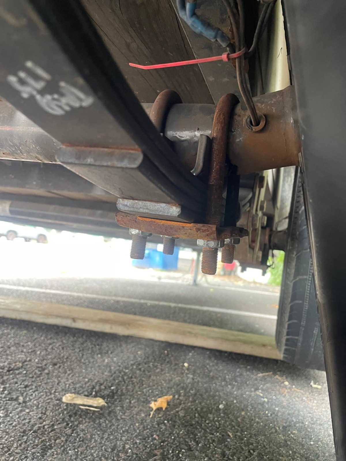 Close-up of rusted trailer U-bolts and leaf-spring hardware during an undercarriage repair