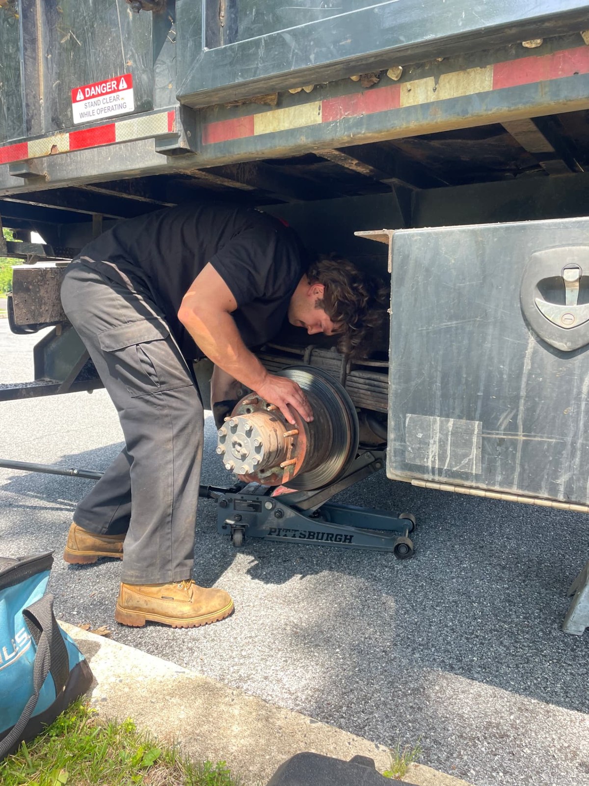 G23 technician replacing a wheel hub and brake assembly on a dump truck raised on a floor jack